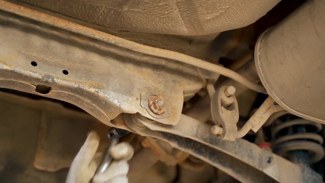 A car mechanic in the inspection pit unscrews the bolt on the car with a wrench. Adjustment of camber and toe. Car suspension repair.