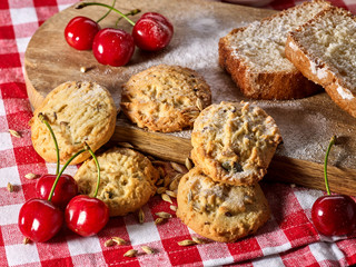 Oatmeal cookies with husk oats and cherry cupcake with powdered sugar on kitchen cutting board gingham checkered cotton fabric on table in village style for picnic.