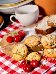 Oatmeal cookies and cherry on kitchen cutting board gingham checkered cotton fabric on table in...