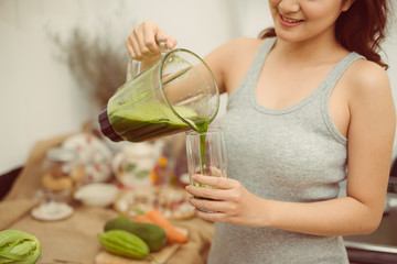 Happy woman pouring a green cocktail into a cup during detox diet