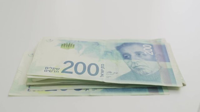 Hand slides Israeli money towards camera then takes it