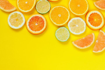 Citrus slices pattern on yellow background from above. Top view of orange, grapefruit, lime and lemon fruit slices on yellow background. Fruit summer cocktail pattern design