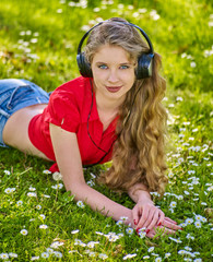 Girl in headphones catch rhythm music on green grass with chamomile flowers summer outdoor. Walking improves memory and concentration.