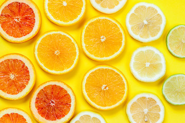 Citrus slices pattern on yellow background from above. Top view of orange, grapefruit, lime and lemon fruit slices on yellow background. Fruit summer cocktail pattern design