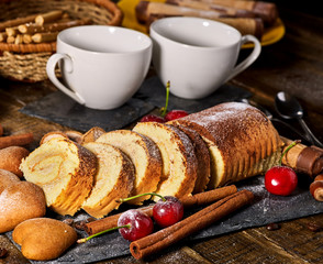 Sand cookies heart shape, rolled cake with cherry and cinnamon stick, coffee cups on kitchen on wooden table in village style. Useful for digestion.