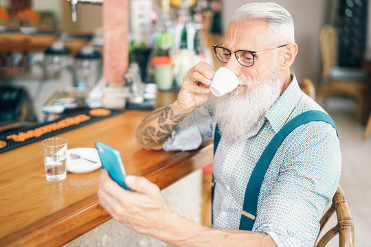 Senior man using mobile smartphone while drinking coffee in bar - Retired male spending time on social networks while having hot drink in restaurant - Technology and elderly people lifestyle concept