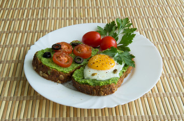 Sandwich with guacamole, egg, olives and tomatoes on a plate
