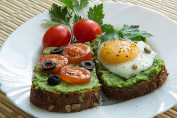 Sandwich with guacamole, egg, olives and tomatoes on a plate