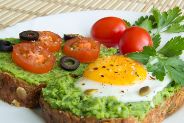 Sandwich with guacamole, egg, olives and tomatoes on a plate