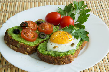 Sandwich with guacamole, egg, olives and tomatoes on a plate
