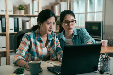 vintage two designers working in company office using laptop computer. group of asian female partner colleagues showing something on screen monitor. woman ceo checking project of employee correcting
