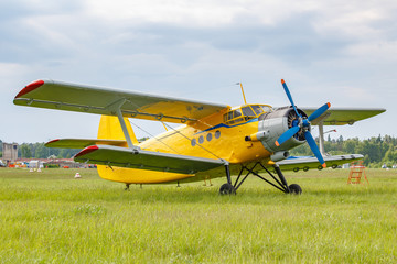 Fototapeta na wymiar Yellow painted legendary soviet aircraft biplane Antonov AN-2 parked on a green grass of airfield against cloudy sky