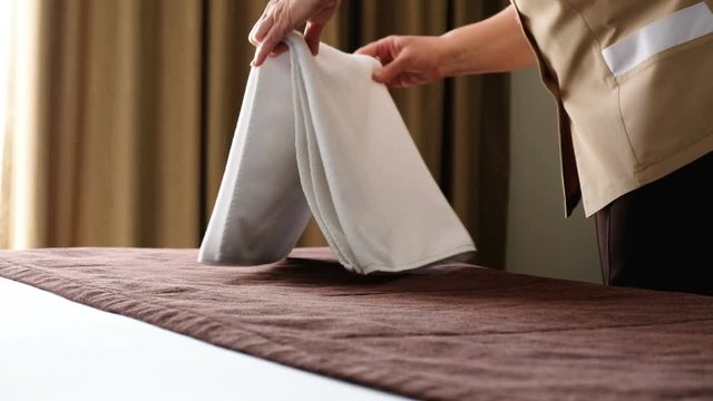 The hands of a middle-aged woman beautifully fold white sheets on the bed of the hotel room. The concept of excellent service in a five-star luxury hotel