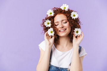 Beautiful curly happy redhead girl posing isolated over purple background with flowers in hair.