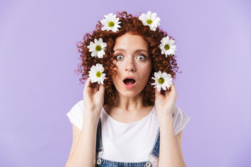 Redhead girl posing isolated over purple background with flowers in hair.