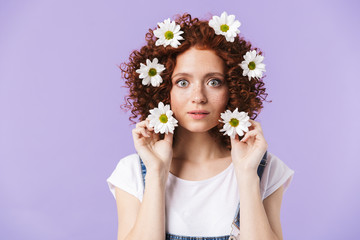 Naklejka premium Redhead girl posing isolated over purple background with flowers in hair.
