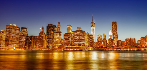 Naklejka premium Downtown Manhattan at night from Brooklyn Bridge Park. New York City skyscrapers reflections in the river