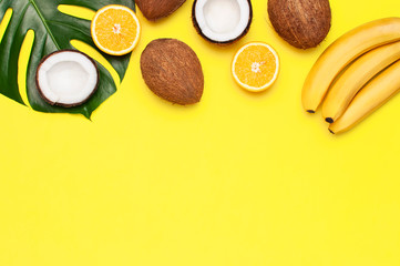 Summer tropical composition. Green tropical leaves of palm trees and monstera, coconut, orange, bananas on bright yellow background. Flat lay, top view, copy space. Creative background food, fruit