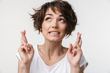 Portrait of joyful woman with short brown hair in basic t-shirt keeping fingers crossed and wishing...