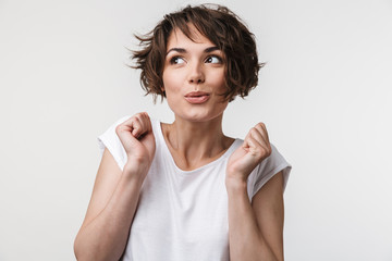 Portrait of excited woman with short brown hair in basic t-shirt rejoicing and clenching fists