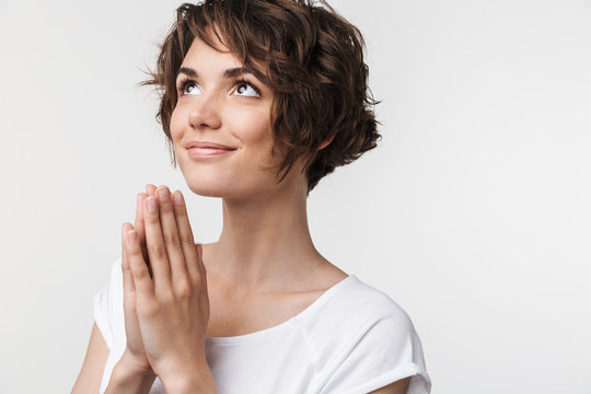 Portrait of confident woman with short brown hair in basic t-shirt keeping palms together and praying