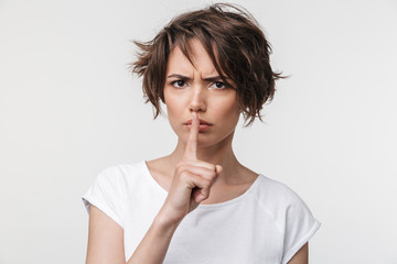 Portrait of angry woman with short brown hair in basic t-shirt holding index finger on lips