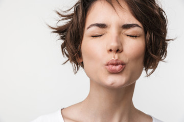Portrait closeup of attractive woman with short brown hair in basic t-shirt making kiss face at...