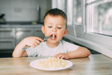 little boy eats pasta in the form of a spiral in the afternoon in the kitchen on their own