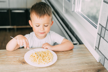 little boy eats pasta in the form of a spiral in the afternoon in the kitchen on their own