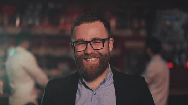 Portrait of smiling attractive man wearing glasses looking at camera in a bar or beer pub. Concept of youth, friendship and resting.
