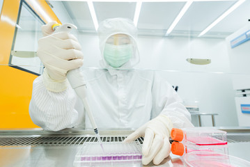 A scientist seeding cells and pipetting growth medium into 96-well plate for molecular assay in...