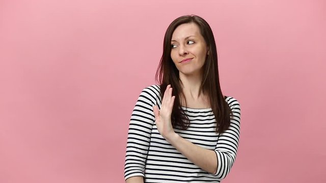 Pretty brunette young woman in striped shirt gesticulating finger like no i do not want that, go away guy, isolated over pastel pink background in studio. People sincere emotions, lifestyle concept.