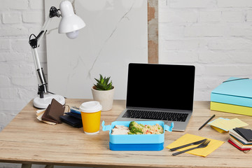lunch box with rice, chicken and broccoli at workplace with laptop on wooden table on white background, illustrative editorial