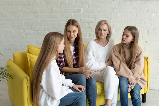 Young beautiful lesbian family in casual clothes sitting on yellow sofa at home