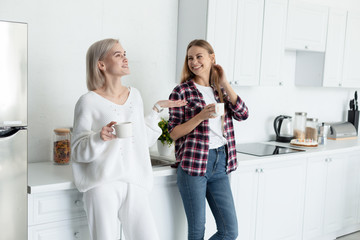 Two young beautiful females in casual clothes spending time together in the kitchen