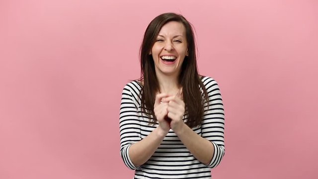 Smiling pretty young woman in striped shirt, fooling, looking at camera with charming smile, inflate cheeks isolated over pastel pink background in studio. People sincere emotions lifestyle concept.