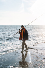 Handsome young man fisherman wearing coat and hat at the seashore.