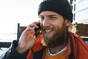 Handsome young man fisherman wearing coat and hat at the seashore talking by phone.