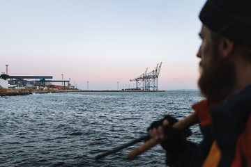 Obraz premium Man fisherman wearing coat and hat standing at the seashore. Focus on sea.