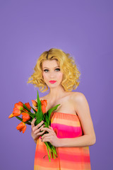 Sexy woman with curly hair and pink lips holds tulips flower. Women's Day. Beauty, fashion concept. Sensual woman with flowers tulips in hands. Attractive girl with bouquet. Florist woman with tulips.