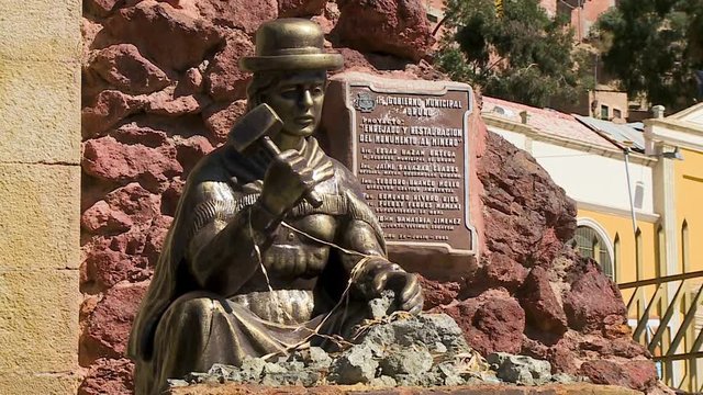 Close-up low-angle still shot of a historic statue of  sad-looking traditionally dressed miner crashing mineral stones, Oruro, Bolivia