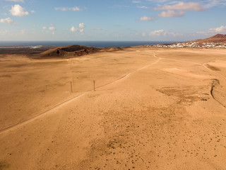 Fototapeta na wymiar Aerial view of a desert landscape on the island of Lanzarote, Canary Islands, Spain. Road that crosses a desert. Reliefs on the horizon. Volcanoes.