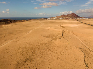 Aerial view of a desert landscape on the island of Lanzarote, Canary Islands, Spain. Road that crosses a desert. Tongue of black asphalt cutting a desert land. Reliefs on the horizon. Volcanoes