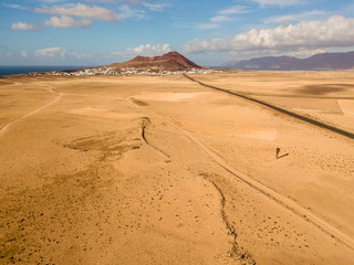 Fototapeta na wymiar Aerial view of a desert landscape on the island of Lanzarote, Canary Islands, Spain. Road that crosses a desert. Tongue of black asphalt cutting a desert land. Reliefs on the horizon. Volcanoes