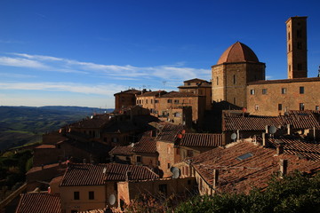 Obraz premium The roofs of the medieval town of Volterra overlook the autumn hills of Tuscany. Satellite dishes, medieval architecture and rustic tiles: epochs mix, just like blue and ochre.