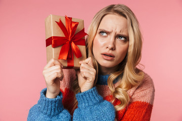 Young pretty beautiful woman posing isolated over pink wall background holding present gift box.