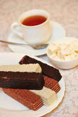 A cup of hot tea and a handful of classic Russian waffles with different fillings on a white surface. Still-life of morning feast, concept sweets for tea