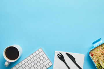 Top view of computer keyboard, cup of coffee, lunch box with delicious meal and disposable fork with knife on blue background