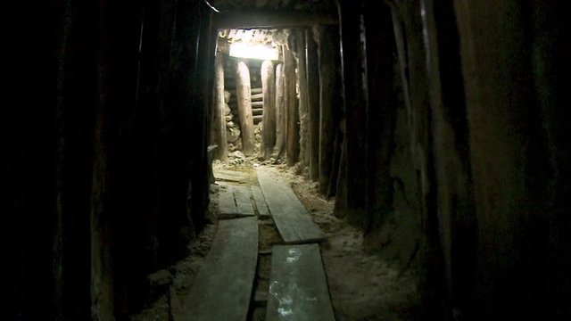 Close-up, low-angle, forward tracking dolly shot of the historic museum mine tunnel supported by thick planks of timber. Overhead ensures vicinity with large flat horizontal floor timber, and
