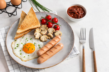 Traditional English Breakfast: sausages, grilled tomatoes and mushrooms, egg, baked beans and bread on the plate on white background. Close up